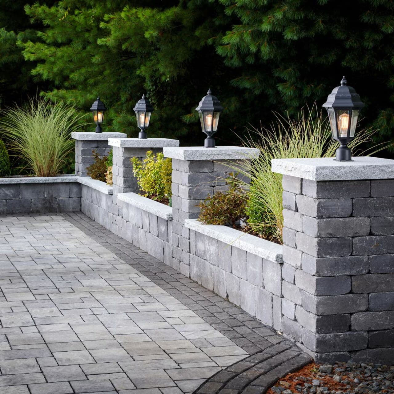 Weston Stone raised garden beds with grasses and shrubs, capped columns with lanterns along a paver patio — Daedalus Contracting, Lower Mainland BC